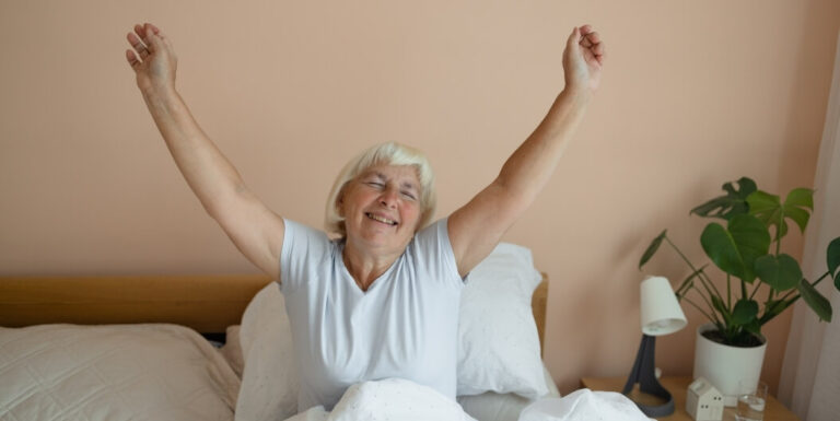 Senior Woman Stretching Happily in Bed at Assisted Living Facility